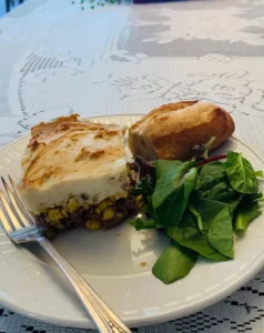 A slice of shepherd's pie on a place next to a baguette and some salad